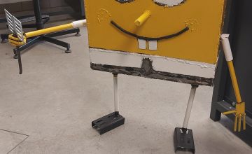 Zdjęcie przedstawiające metalową rzeźbę w kształcie żółtego prostokąta z nogami i rękami